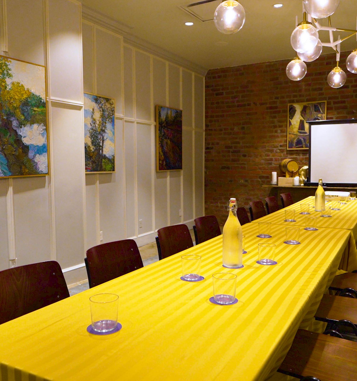 Conference room with a long table, chairs, art on walls, and a projection