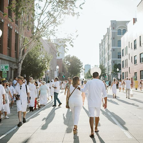 A couple walks down a street where many people are dressed in white.