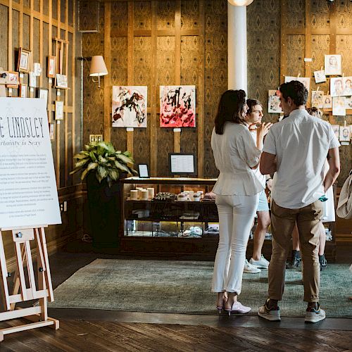 People at an event with artwork displayed on walls and easel signage.