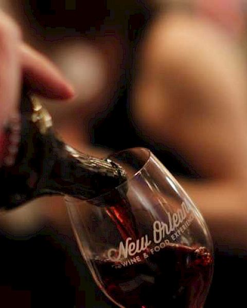 A person's hand is pouring red wine into a glass with a logo.